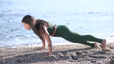 Yoga eğitmeni yunus hareketi yapıyor. Huzurlu bir plajda, sağlığını ve farkındalığını arttırıyor.