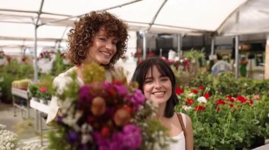 Gülümseyen kadınlar renkli çiçek odasında taze buket gösteriyorlar.