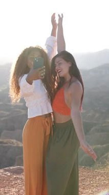 İki arkadaş selfie çekmekten ve birlikte gülmekten zevk alır çarpıcı bir günbatımı arkaplanına karşı, doğada dostluk ve macera sergilerler.