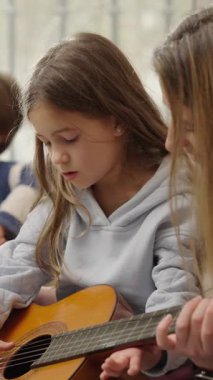 Özel akustik dersi sırasında genç kız öğrencilere gitar çalma becerilerini geliştirmede rehberlik ediyor.