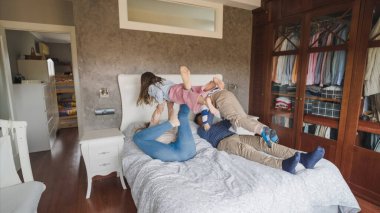 Aile üyeleri rahat bir yatak odasındaki yatakta oynarken eğleniyor ve kaynaşıyorlar. Ev ortamında neşe ve beraberlik sergiliyorlar.