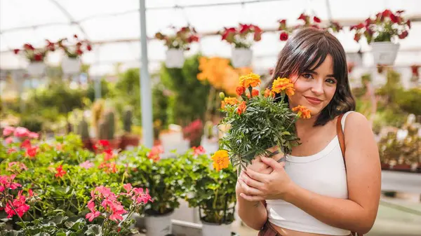 Genç bahçıvan renkli çiçeklerle çevrili bir serada Fransız kadife çiçeği tutuyor.