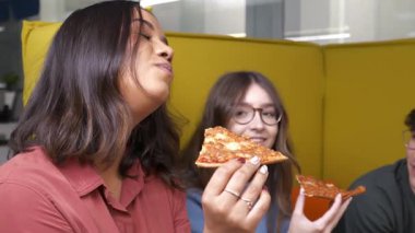 Bir grup bayan meslektaşım sarı koltukta dinleniyor, günlük iş yemeği molasında leziz pizza dilimlerinin tadını çıkarıyor ve ortak bir keyif ve iş arkadaşlığı paylaşıyorlar.