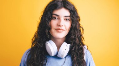 Boynunda kulaklıklarla genç ve kendinden emin bir öğrencinin portresi, canlı sarı bir arka plana hafifçe gülümsüyor.