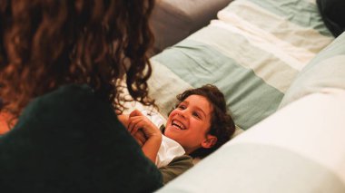 Mutlu çocuk gülüyor ve annesiyle neşeyle oynuyor. Yatakta rahat bir şekilde uzanırken. Sevgi ve bağlantının değerli anlarını paylaşıyor.