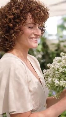 Beyaz çiçeklerle çalışan profesyonel bir kadın çiçekçi. Seranın içinde güzel kokulu çiçeklerin tadını çıkarırken, elinde zarif bir buket çiçek tutuyor. Dikey