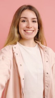 Gülümseyen genç bir kadın siyah bir kağıda sarılıp kırmızı bir fiyonkla pembe bir arka planda izole edilmiş bir hediye sunuyor.