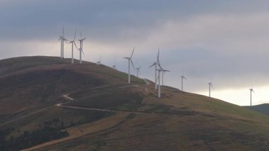 Yeşil yamaçta dönen rüzgar türbinleri, Cantabria kırsalındaki bulutlu gökyüzünün altında sürdürülebilir güç gelişimini temsil eden yenilenebilir enerji üretir.