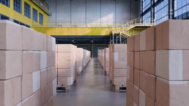 Kamera büyük, modern bir lojistik deposunda hareket ediyor. Ahşap paletler üzerinde yığılı karton kutular nakliyeye hazır.