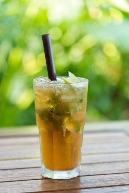 Naneli limonlu buzlu çay, limon suyu ve şekerli siyah çay, limon dilimleri ile süslenmiş ve tahta masada nane şekeri, doğa arka planı, sağlıklı bir yaz içeceği..