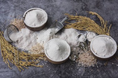 Pirinç unu Tayland unu organik bir kaşık içinde ahşap bir kase ile beyaz pirinç yığını, çeltik kulağı ve beton arka planda süzgeç, üst manzara düzlüğü, yiyecek ve pişirme malzemeleri..