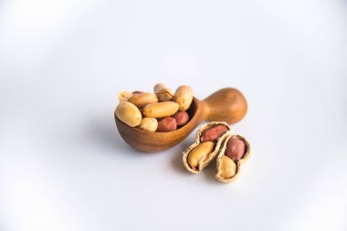 Tahta kaşıkta yer fıstığı kabuklarında yer fıstığı ve kabuksuz birkaç tane. Protein açısından zengin, beyaz arka planda izole edilmiş fıstıklı sağlıklı atıştırma konsepti..