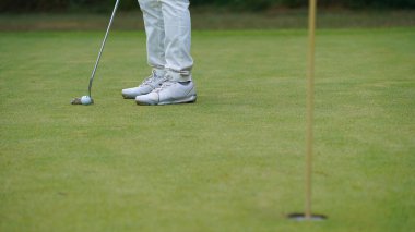 Golfçü topu yeşil golfün üstüne koyuyor, mercek akşam vakti parlıyor. Golfçü vuruşu uzun süre deliğe soktuktan sonra kazanır..                                  