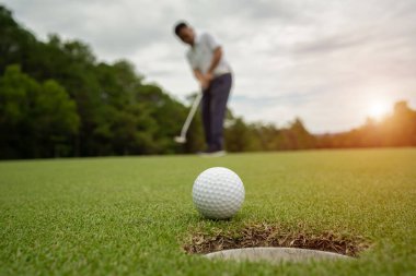 Golf sahasında golf sahasının üzerine beyaz golf topu yuvarlanıyor. Golf sahasının arka planında ve bulanık golfçüler turnuvanın galibiyetini kutluyor..