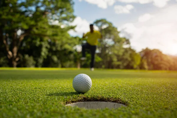 ホワイトゴルフボールローリングダウンゴルフホールで緑を入れます夜のゴルフコースの背景とぼやけたゴルファーは優勝トーナメントで祝う — ストック写真