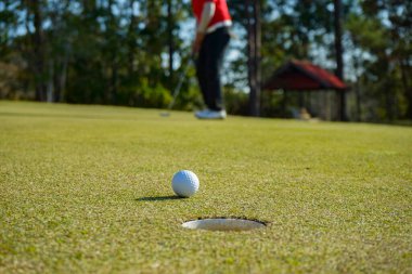 Golfçü topu yeşil golfün üstüne koyuyor, mercek akşam vakti parlıyor. Golfçü vuruşu uzun süre deliğe soktuktan sonra kazanır..                                 