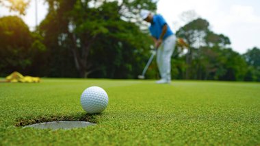 Golfçü topu yeşil golfün üstüne koyuyor, mercek akşam vakti parlıyor. Golfçü vuruşu uzun süre deliğe soktuktan sonra kazanır..                                