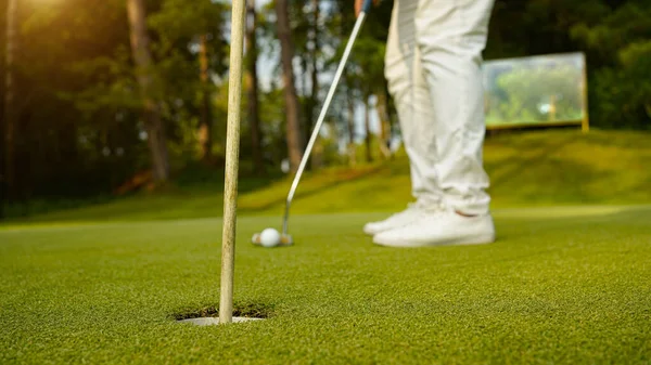 夕日の緑の芝生のゴルフコースでゴルファーによって穴になるだろうゴルフボール ゴルファーは夕方のゴルフコースにゴルフを入れています 日没の夜の時間に — ストック写真
