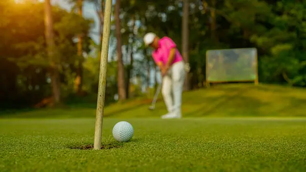 緑のゴルフにボールを入れてゴルファー 太陽の下でレンズフレアは夜の時間を設定します 長い穴にゴルフボールを入れて後に勝つためにゴルファーのアクション — ストック写真