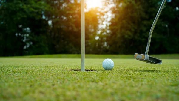 夕日の緑の芝生のゴルフコースでゴルファーによって穴になるだろうゴルフボール ゴルファーは夕方のゴルフコースにゴルフを入れています 日没の夜の時間に ストック画像