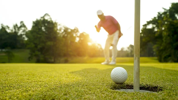 緑のゴルフにボールを入れてゴルファー 太陽の下でレンズフレアは夜の時間を設定します 長い穴にゴルフボールを入れて後に勝つためにゴルファーのアクション ロイヤリティフリーのストック写真
