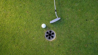 Yeşil sahada golf sopası olan bir golf topunun en üst görüntüsü. Golf topu ve golf sopası akşam golf sahasında güneş ışığı altında..                               