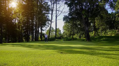 Golfçü topu yeşil golfün üstüne koyuyor, mercek akşam vakti parlıyor. Golfçü vuruşu uzun süre deliğe soktuktan sonra kazanır..                                