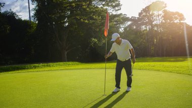Golf sahasında gün batımında golf sahasında bayrak deliğini tutan bir golfçü..                                