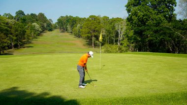 Golfçü golf oynuyor ve yeşil çimen dağ arka planına vuruyor. Asya 'lı erkek oyuncu yazın vuruldu. Spor tatil yaşam tarzı konsepti.                               