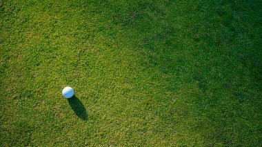 Golf topu yeşil çimlerin üzerinde, golf sahasında, arka planda güneş ışığı var. Yeşil çimlerin üzerindeki deliğin kenarındaki golf topu sıcak bir tonla ve günbatımıyla..                               
