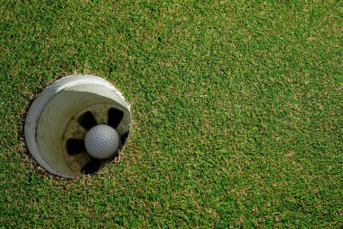 Seçici odaklanma. Yeşil çimlerin üzerinde delikte güneş ışığı olan beyaz golf topu..                                 