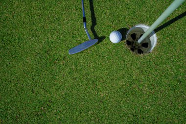 Yeşil sahada golf sopası olan bir golf topunun en üst görüntüsü. Golf topu ve golf sopası akşam golf sahasında güneş ışığı altında..                                