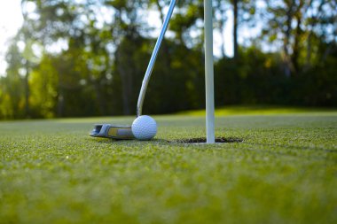 Yeşil sahada golf sopası olan bir golf topunun en üst görüntüsü. Golf topu ve golf sopası akşam golf sahasında güneş ışığı altında..                                