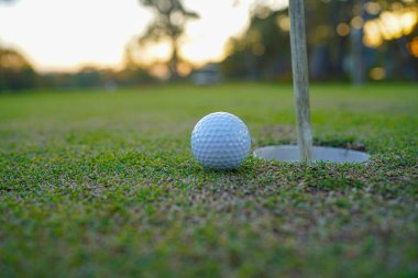 Golf topu deliğin yanında ve bayrak golf sahasında akşam golf sahasında güneş ışığı altında..                         