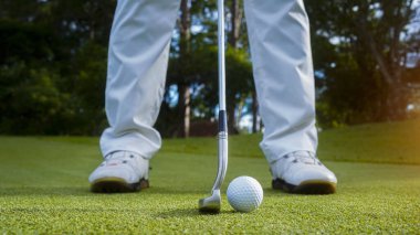 Golfçü topu yeşil golfün üstüne koyuyor, mercek akşam vakti parlıyor. Golfçü golf topuna vuruyor. Spor tatil yaşam tarzı kavramı.                               