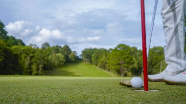 Golfçü topu yeşil golfün üstüne koyuyor, mercek akşam vakti parlıyor. Golfçü golf topuna vuruyor. Spor tatil yaşam tarzı kavramı.                               