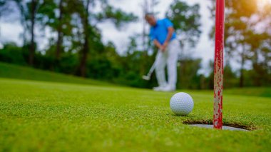 Golfçü topu yeşil golfün üstüne koyuyor, mercek akşam vakti parlıyor. Golfçü golf topuna vuruyor. Spor tatil yaşam tarzı kavramı.                               