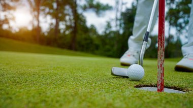 Golfçü topu yeşil golfün üstüne koyuyor, mercek akşam vakti parlıyor. Golfçü golf topuna vuruyor. Spor tatil yaşam tarzı kavramı.                               