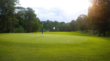 Golfçü topu yeşil golfün üstüne koyuyor, mercek akşam vakti parlıyor. Golfçü golf topuna vuruyor. Spor tatil yaşam tarzı kavramı.                               