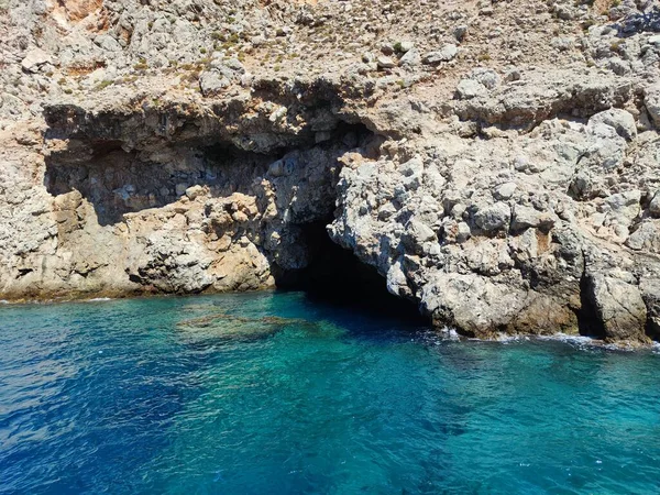 Stock image Clear blue sea splashing on grey rock formation in bright sunlight