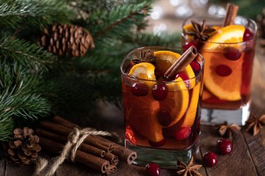 Portakal dilimli sıcak şarap, kızılcık ve baharatlar kırsal ahşap masa üzerinde ve arka planda Noel ağacı süslemesi
