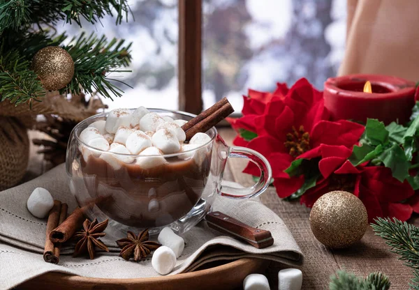冬の背景を持つウィンドウで木製のテーブルの上に休日の装飾を持つマシュマロとシナモンとホットチョコレートのカップ — ストック写真