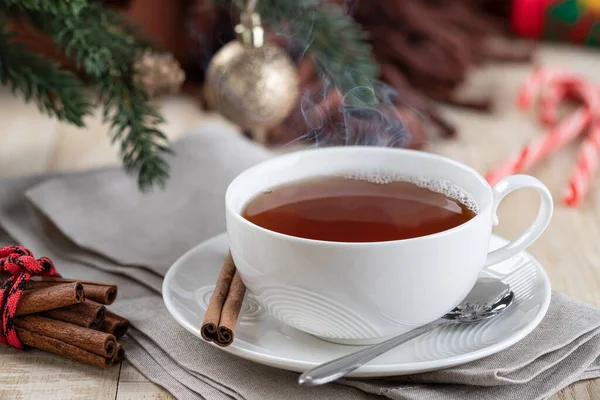 Steaming hot cup of tea on a wooden table with Christmas decorations in background