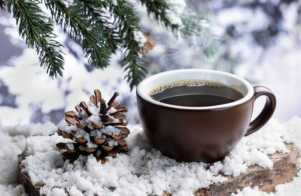 Steaming hot cup of coffee on a snow covered tree stump with a winter background