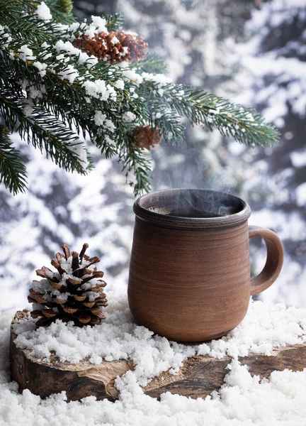 Steaming hot cup of coffee on a snow covered tree stump with a winter forest background