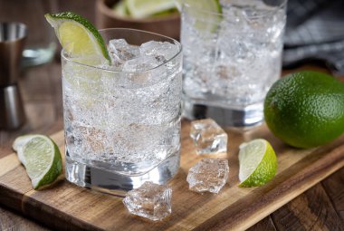 Gin and tonic cocktail with lime slices, and ice on a wooden board