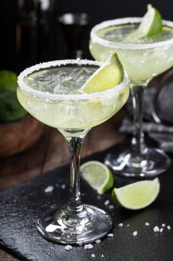 Margarita cocktail with ice, lime and salt rim on a black slate board 