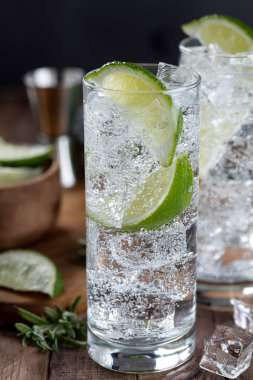 Closeup of gin and tonic cocktail with lime slices, and ice on a rustic wooden table