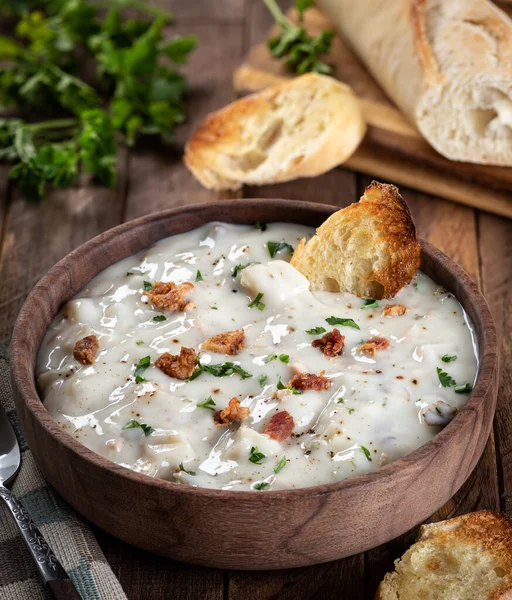 New england clam chowder with bacon, parsley and toasted french bread in a wooden bowl