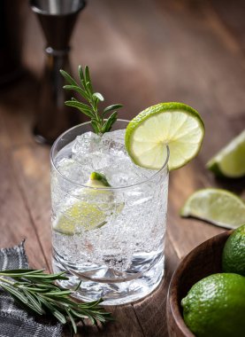 Gin and tonic cocktail with lime slices, rosemary and ice on a rustic wooden table.  High angle view and copy space